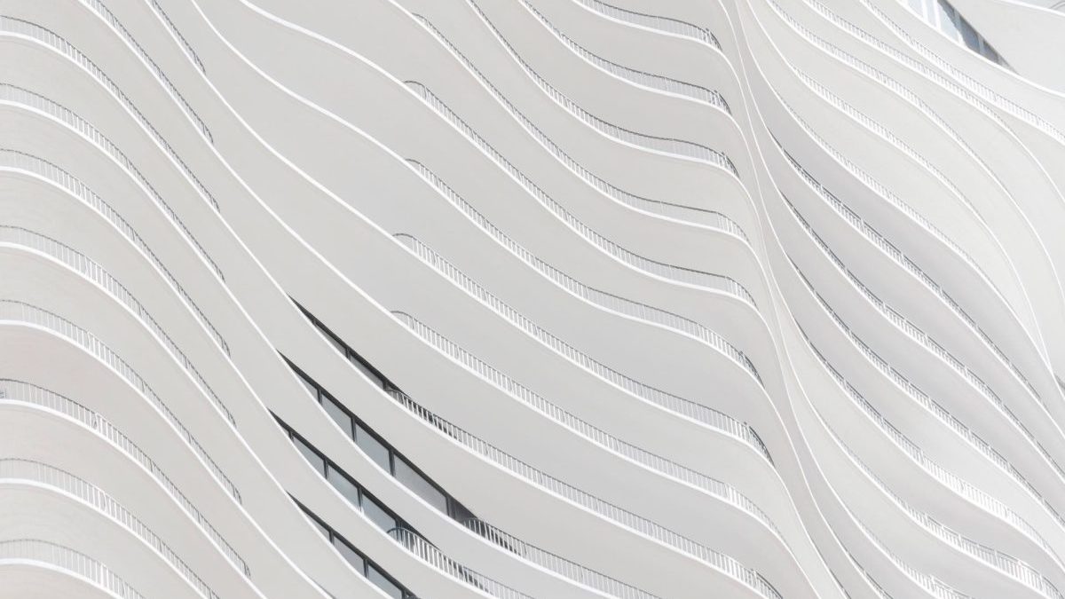 Abstract view of a modern building facade featuring flowing, wavy white lines and narrow windows, creating a sense of movement and repetition.