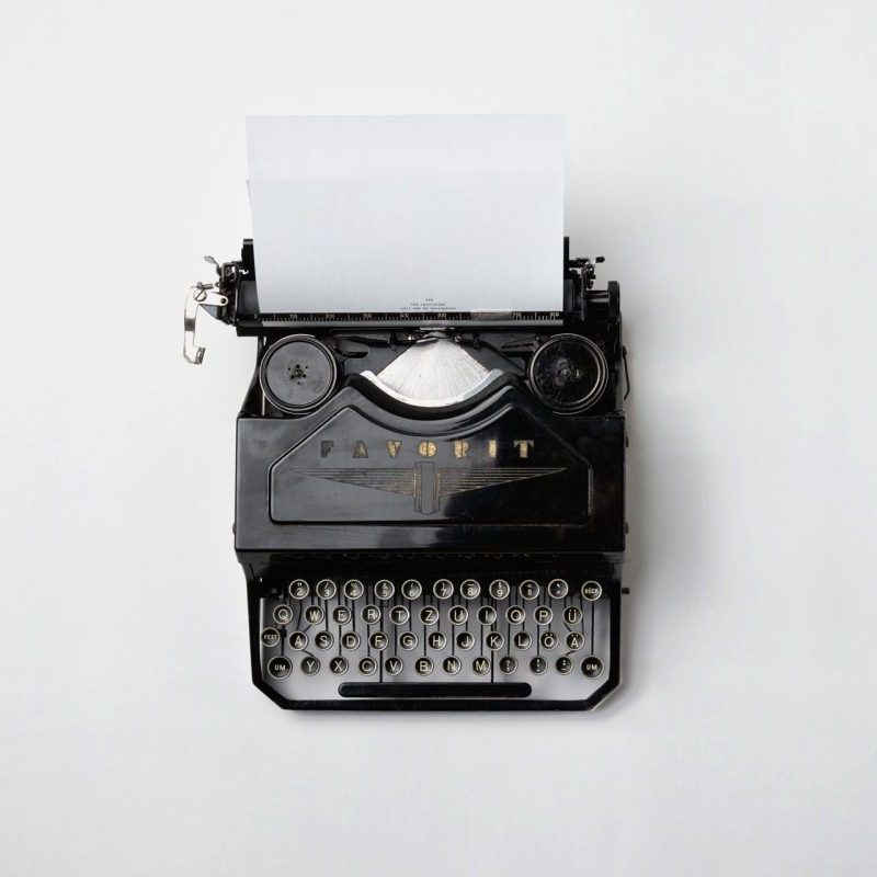 A black vintage typewriter with a blank sheet of paper loaded, photographed from above on a plain white background.