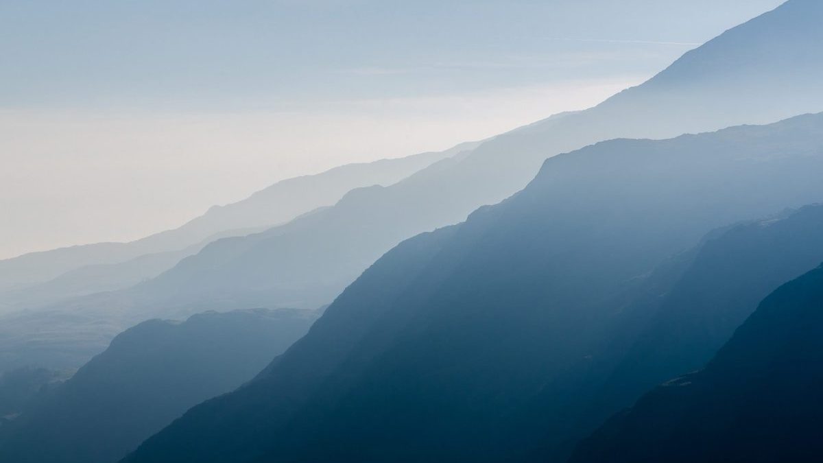 A series of mountain ridges in soft blue hues, layered and fading into the misty distance under a hazy sky.