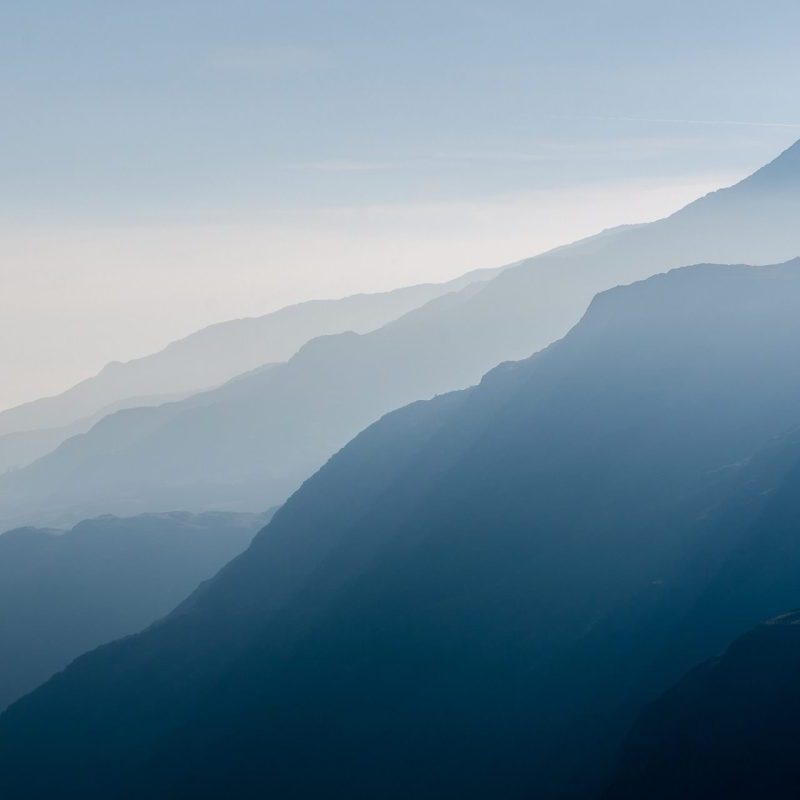 A series of mountain ridges in soft blue hues, layered and fading into the misty distance under a hazy sky.