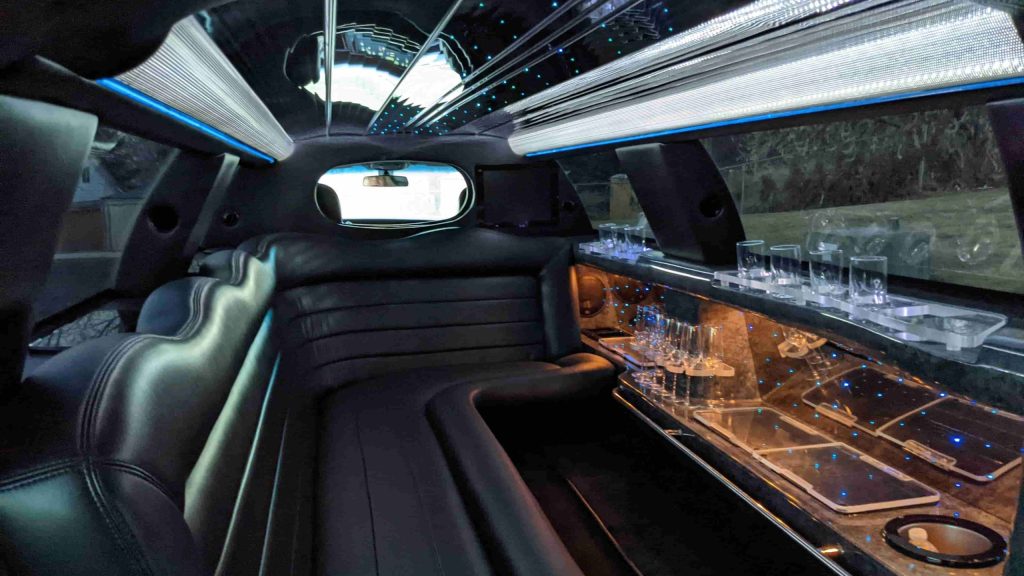 Interior of a luxury limousine showcases plush leather seats, a small bar area with glasses, mirrored surfaces, and ambient ceiling lights—just some of the refined amenities you can expect inside.