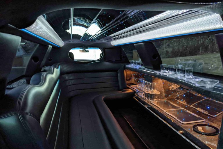 Interior of a luxury limousine showcases plush leather seats, a small bar area with glasses, mirrored surfaces, and ambient ceiling lights—just some of the refined amenities you can expect inside.